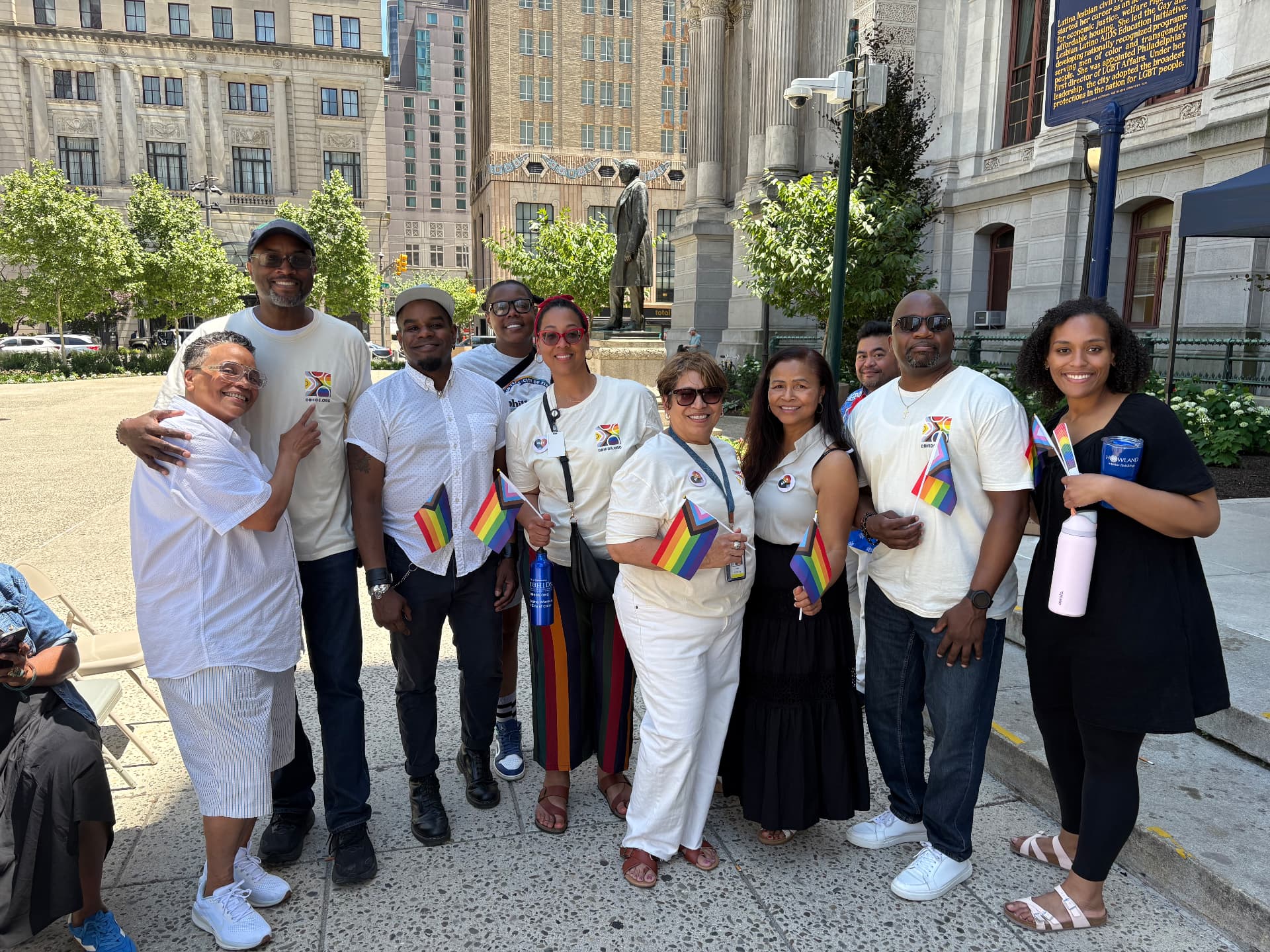 A diverse group of wellness program participants gathers with pride flags outside Philadelphia City Hall.
