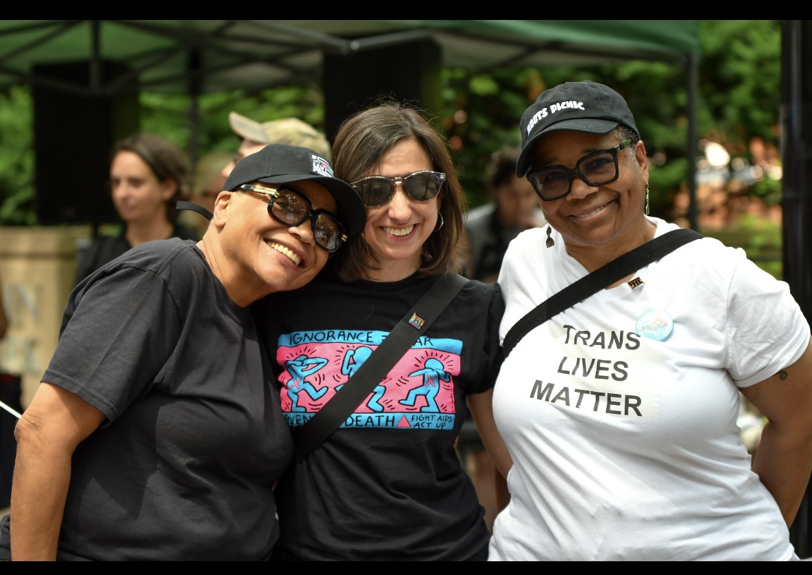 Community members smile and embrace at an outdoor Pride event, celebrating trans lives.
